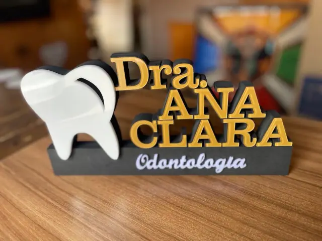 Display de mesa com dente branco e nome de dentista em letras douradas