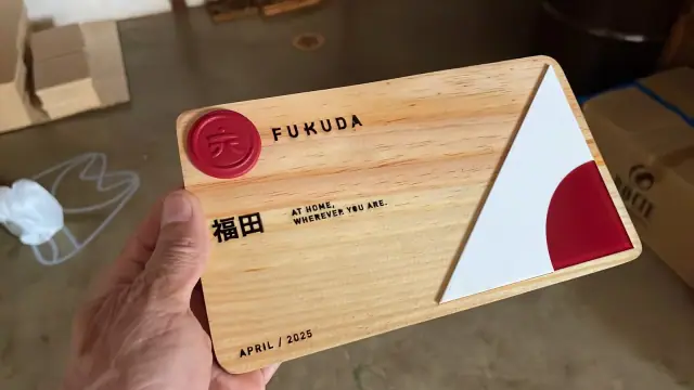 Placa retangular de aspecto amadeirado com logo Fukuda e detalhes vermelhos