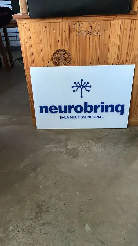 Placa branca com logotipo azul da Neurobrinq apoiada na oficina